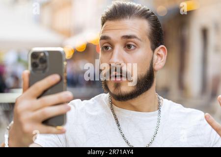 Oh mon Dieu Wow. Heureux heureux heureux heureux gagnant barbu jeune homme utiliser smartphone dactylographie navigation célébrer gagner bonne nouvelle de message. Homme avec téléphone mobile marchant dans la ville ensoleillée urbaine rue à l'extérieur Banque D'Images