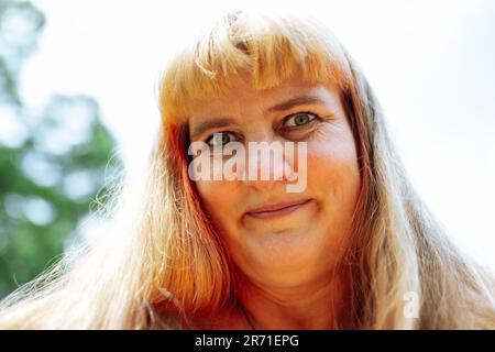 Portrait bonne souriante femme d'âge moyen avec de longs cheveux blonds sur un arrière-plan flou de la lumière du soleil Banque D'Images