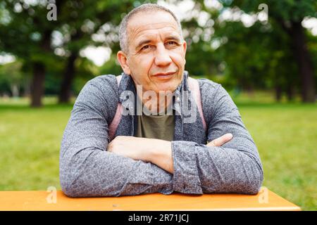 Beau homme d'âge moyen, aux yeux bruns, aux cheveux gris, gros plan sur un parc d'été vert flou Banque D'Images