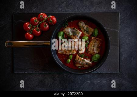 Faites frire le poisson frit dans une sauce tomate épicée sur fond sombre. Éclairage faible Banque D'Images