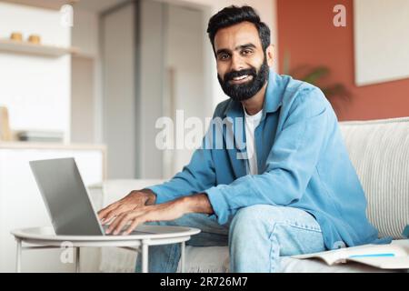 Homme arabe souriant travaillant sur un ordinateur portable assis dans le salon Banque D'Images
