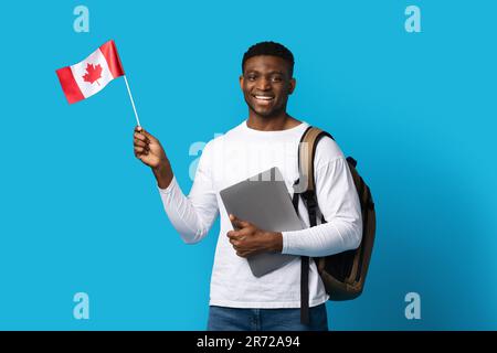 Un étudiant africain positif tenant un ordinateur portable et un drapeau canadien Banque D'Images