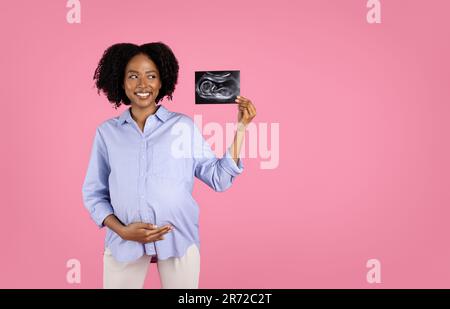 Bonne jeune enceinte afro-américaine cally femme en décontracté avec grand ventre montrer échographie shot Banque D'Images