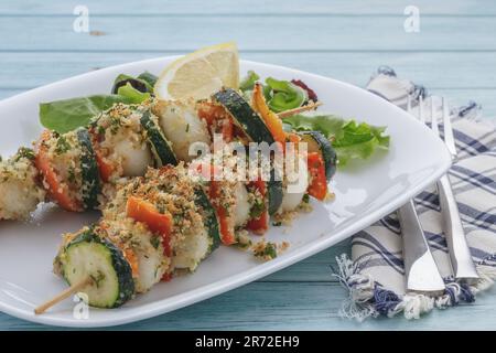Brochettes de poisson et de légumes, sur une assiette de service décorée de citron et de salade Banque D'Images