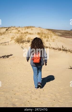 Femme aux cheveux longs avec un sac à dos qui marche sur les dunes de sable. Banque D'Images