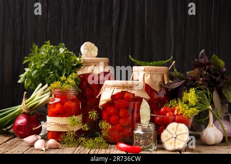 Tomates cerises marinées avec ail, aneth et épices. Tomates en conserve faites maison en pots fermés avec couvercles artisanaux, poivrons chauds frais et tomates Banque D'Images