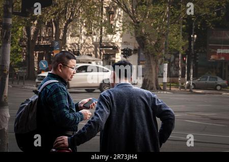 Photo de deux hommes, touristes, Asiatiques de Chine, assis et utilisant leurs smartphones pour utiliser des applications sur un réseau Internet wifi public dans une rue Banque D'Images