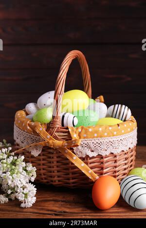 Panier en osier avec des œufs de Pâques décorés avec soin et des fleurs de lilas blanc sur une table en bois Banque D'Images