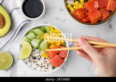 Femme mangeant un délicieux poke Bowl avec du saumon, de la chaux et des légumes sur une table en marbre blanc, vue du dessus Banque D'Images