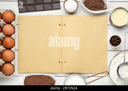 Livre de recettes vierge entouré de différents ingrédients sur une table en bois blanc, plat. Espace pour le texte Banque D'Images
