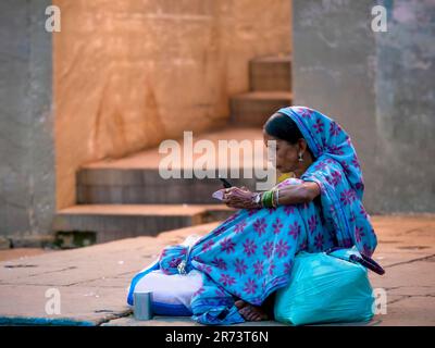 Varanasi, Inde - 11 novembre 2015. Une femme indienne âgée portant un sari traditionnel et un foulard utilise un téléphone portable tout en étant assise à l'extérieur. Banque D'Images
