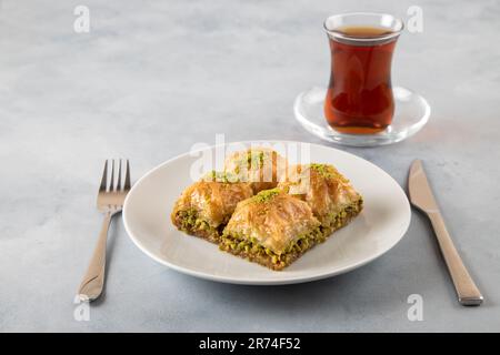 Pistache baklava sur une assiette blanche avec thé turc. Baklava turque traditionnelle et thé sur fond bleu clair Banque D'Images