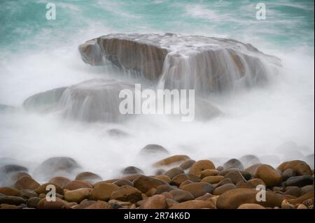 Les vagues blanches s'écoulent lentement des rochers vers la mer. Prise de vue en exposition lente. Vue sur le port de Keelung depuis la plage de Wanli à New Taipei. Taïwan. Banque D'Images