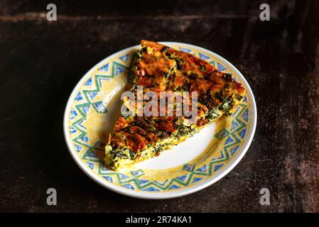 Morceau de tarte aux épinards et au fromage fraîchement préparés sur une assiette sur fond sombre. Tarte végétalienne. Banque D'Images