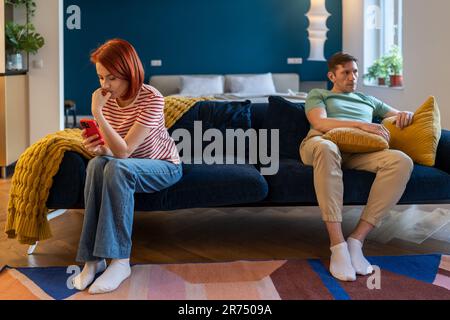 Couple homme et femme ignorant l'un l'autre, femme au téléphone mari assis près sur le canapé. Banque D'Images