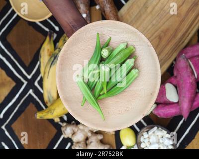 une femme africaine hache des légumes aux fruits d'okra pour cuisiner une recette traditionnelle avec d'autres légumes et fruits locaux. Banque D'Images