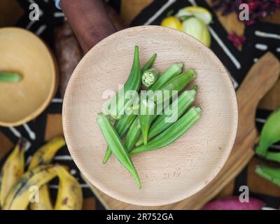 une femme africaine hache des légumes aux fruits d'okra pour cuisiner une recette traditionnelle avec d'autres légumes et fruits locaux. Banque D'Images