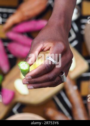 une femme africaine hache des légumes aux fruits d'okra pour cuisiner une recette traditionnelle avec d'autres légumes et fruits locaux. Banque D'Images