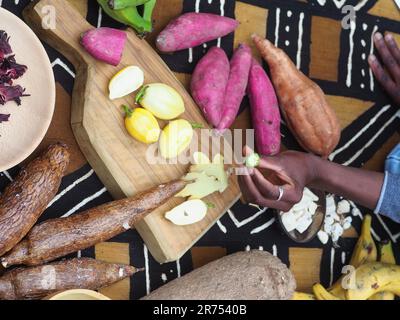 une femme africaine hache des légumes aux fruits d'okra pour cuisiner une recette traditionnelle avec d'autres légumes et fruits locaux. Banque D'Images