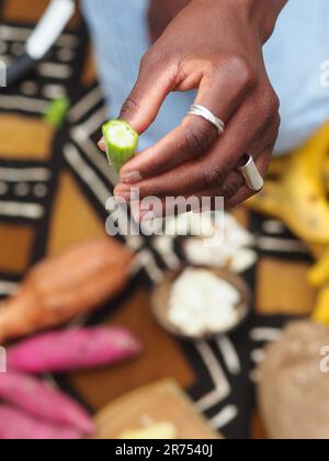 une femme africaine hache des légumes aux fruits d'okra pour cuisiner une recette traditionnelle avec d'autres légumes et fruits locaux. Banque D'Images