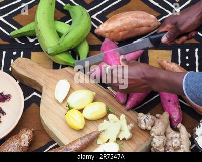 femme noire coupant des légumes et des fruits africains typiques, coup de tête. Cuisine de la côte d'Ivoire. Banque D'Images