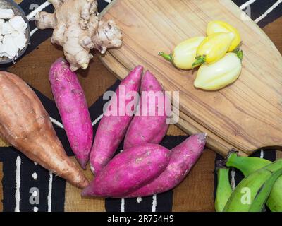 Femme noire tenant de la pomme de terre rouge sucrée africaine, d'autres ingrédients locaux à l'arrière-plan pour la cuisine traditionnelle de recette Banque D'Images