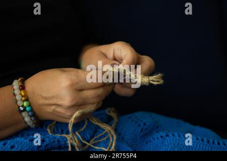 Les mains d'une femme et le fil de jute et le fragment d'un motif tricoté. tricot écologique naturel, artisanat et passe-temps, décoration écologique. Banque D'Images