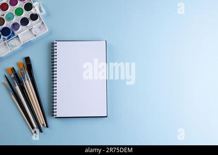 Gros plan des peintures, des carnets et des pinceaux avec espace de copie sur fond bleu. Retour à l'école, art, peinture, matériel scolaire, apprentissage, école et edu Banque D'Images