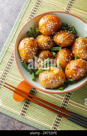 Pommes de terre glacées servies avec des oignons verts et des graines de sésame dans un bol sur la table. Vue verticale du dessus Banque D'Images