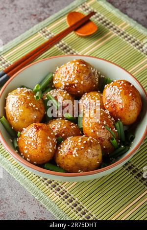 Pommes de terre glacées servies avec des oignons verts et des graines de sésame dans un bol sur la table. Verticale Banque D'Images