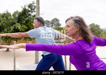 Couple aîné caucasien avec les bras tendus pratiquant la pose de yoga guerrier 2 à la plage Banque D'Images