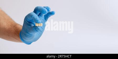 La main du médecin en gants bleus tient un modèle de dent sur un blanc Banque D'Images