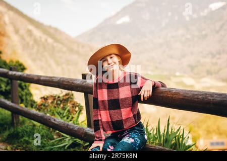 Portrait extérieur d'une jeune fille à cheveux rouges portant un chapeau marron, randonnée en montagne, assise sur la clôture Banque D'Images