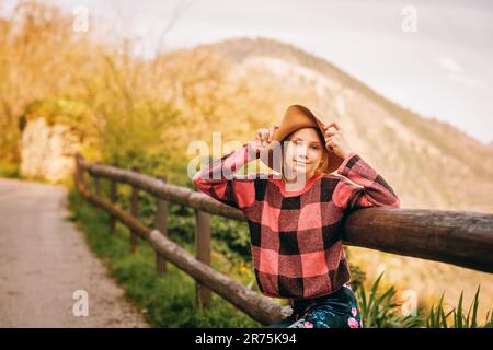 Portrait extérieur d'une jeune fille à cheveux rouges portant un chapeau marron, randonnée en montagne, assise sur la clôture Banque D'Images