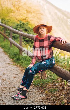 Portrait extérieur d'une jeune fille à cheveux rouges portant un chapeau marron, randonnée en montagne, assise sur la clôture Banque D'Images