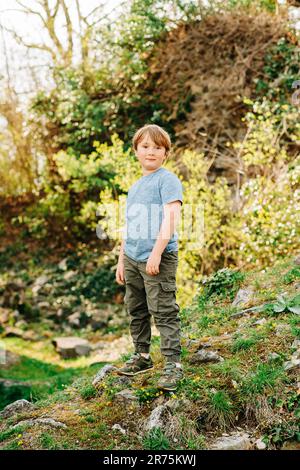 Joli petit garçon jouant dans le parc d'été, fond vert nature, portant un t-shirt bleu et pantalon kaki Banque D'Images