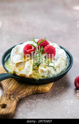 Camembert cuit au four avec feuilles de romarin et framboise. brie grillée maison sur une table rustique. Banque D'Images