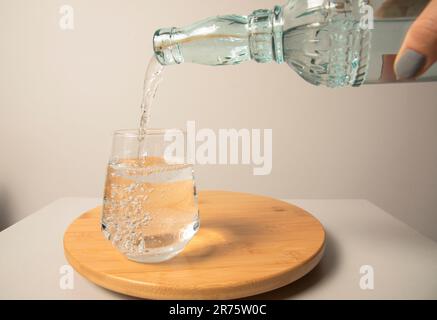 Verser en gros plan de l'eau de boisson fraîche purifiée de la bouteille. Surface en bois Banque D'Images