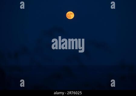 Pleine lune s'élevant dans un ciel bleu foncé au-dessus de la côte sud de Cornwall , Angleterre avec l'océan en dessous Banque D'Images