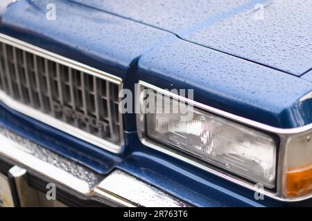 Izmir, Turquie - 3 juin 2023 : gros plan du phare unique sur un Caprice de Chevrolet bleu, peut-être un modèle 1978, orné de gouttes de pluie Banque D'Images