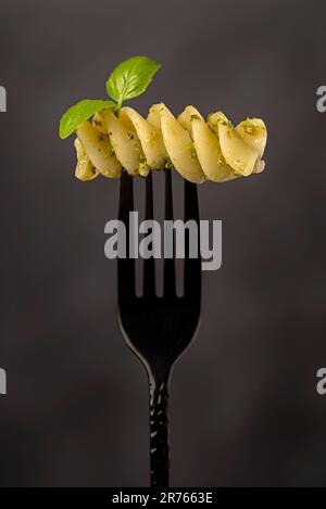 Macro-photographie alimentaire de fusilli géant, pâtes, basilic, pesto, sauce, huile d'olive, parmesan, fromage, semoule de blé dur, fourchette, arrière-plan Banque D'Images