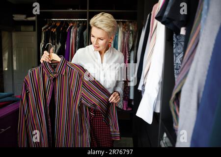 La styliste de femme mature organise ou choisit une tenue de vêtements et essaie dans le grand placard à la maison. Banque D'Images