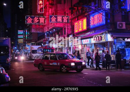 Mong Kok, Hong Kong - 12 avril 2023: Un taxi rouge traditionnel et des panneaux de néon colorés Banque D'Images
