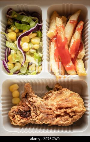 La boîte à bento contient des cuisses de poulet, des frites et de la salade de légumes. Banque D'Images