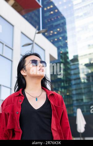 Jeune femme attentionnés avec une tenue décontractée et des lunettes de soleil qui donnent sur l'extérieur tout en marchant dans la rue avec des bâtiments modernes pendant le week-end Banque D'Images