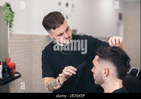 Jeune barbier peignant homme dans le salon de coiffure sur fond flou Banque D'Images