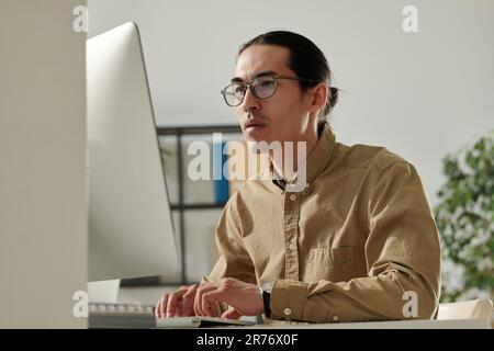 Jeune homme d'affaires asiatique regardant les données financières en ligne sur écran d'ordinateur tout en l'analysant et en préparant le rapport pour le séminaire Banque D'Images