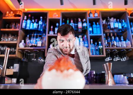 Jeune shaker offrant un cocktail spécial et coloré à ses clients. Concept: Boissons, consommation, vie nocturne Banque D'Images