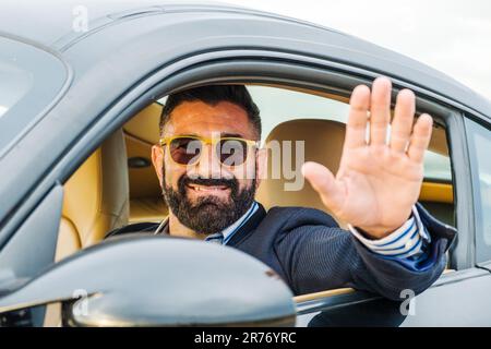 Un jeune homme souriant dans des lunettes de soleil vagues de sa voiture Banque D'Images