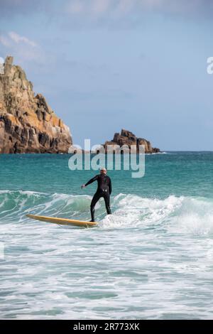 Surfer dans la mer à la plage de Porthcurno à Cornwall, Angleterre, Royaume-Uni Banque D'Images